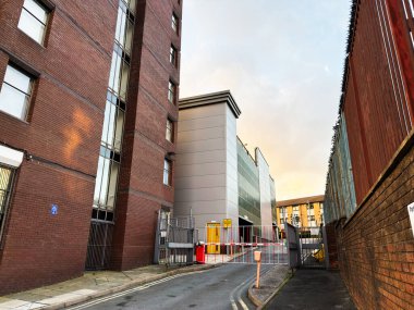 Salford, İngiltere - 08 Kasım 2025: Tuğla binalar arasındaki dar bir sokak bir güvenlik kapısının arkasındaki çağdaş ek binaya çıkıyor.