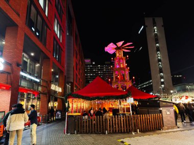 Manchester, İngiltere - 08 Kasım 2025: Kalabalık Manchester 'da renkli bir kulenin yanındaki dekoratif ışıkların altında toplanıyor.