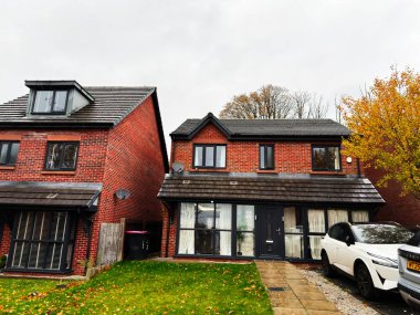 Manchester, İngiltere - 9 Kasım 2025: Manchester 'da garaj yolu, park edilmiş araba ve sonbahar yeşilliği olan üç katlı kırmızı tuğlalı ev.