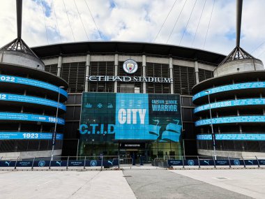Manchester, İngiltere - 16 Kasım 2025: Manchester 'da canlı bir futbol stadyumu, mavi pankartlar, cam cephe ve ekranlar.