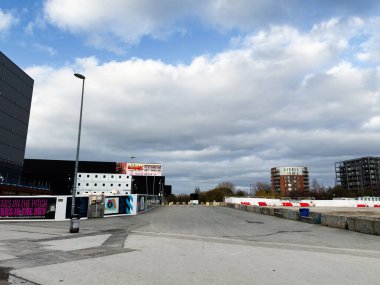 Manchester, İngiltere - 16 Kasım 2025: Yeni kalkınma, bulutlu gökyüzü, sokak lambaları ve Manchester 'daki bariyerlerin yanında boş asfalt alan.