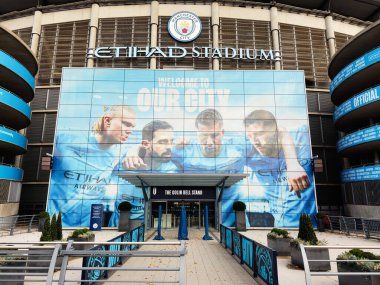 Manchester, İngiltere - 16 Kasım 2025: Dev bir mavi bayrak ve ana girişi olan Manchester City stadyumunun dış görünüşü.