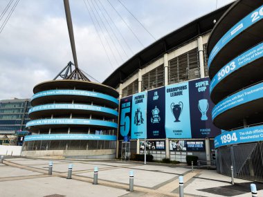 Manchester, İngiltere - 16 Kasım 2025: Manchester City Stadyumu 'nun mavi bayrakları ve dairesel heykeli.
