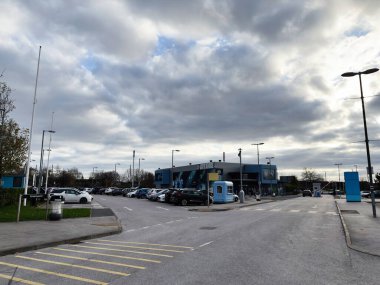 Manchester, İngiltere - 16 Kasım 2025: Manchester Stadyumu yakınlarındaki otopark, mavi binalar ve bulutlu gökyüzüyle gösteriliyor.