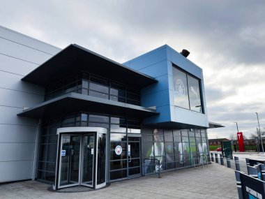 Manchester, İngiltere - 16 Kasım 2025: Çağdaş şehir spor salonu cam cephe, döner kapılar ve kalın mavi paneller.