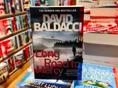 Manchester, İngiltere - 15 Kasım 2025: Renkli roman ve kitaplarla çevrili, hareketli bir kitapçı rafında bir Baldacci kapağı.