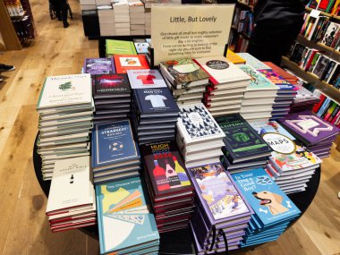 Manchester, İngiltere - 15 Kasım 2025: Yoğun bir kitapçıda yuvarlak bir masaya yığılmış renkli kitap çeşitleri, okumaya davet.