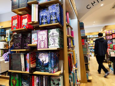 Manchester, İngiltere - 15 Kasım 2025: Canlı kapaklı, uzun ahşap raflı ve seçimleri keşfeden müşterilerle dolu kitapçı sahnesi.