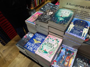 Manchester, İngiltere - 15 Kasım 2025: Bir kitapçıda yığılmış kitapların canlı gösterisi, okurları fantezi ve romantizm başlıklarını keşfetmeye davet ediyor.