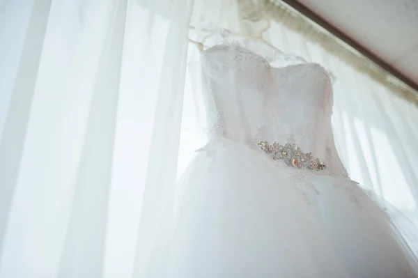 Beautiful white wedding gown hanging by window — Stock Photo, Image