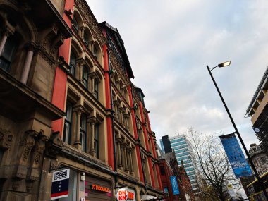 Manchester, İngiltere - 16 Kasım 2025: Dekoratif mimarisi, dükkan önleri, afişleri ve modern gökyüzü çizgisi ile kalabalık bir Manchester şehri caddesi.