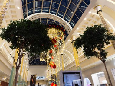 Stretford, İngiltere - 15 Kasım 2025: Altın avizeler, Noel süsleri ve Trafford Center Manchester alışveriş merkezi içindeki yemyeşil ağaçlar ile şık bir tatil gösterisi.