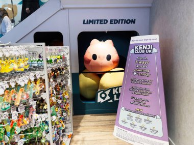 Stretford, İngiltere - 15 Kasım 2025: Renkli anahtarlıklar ve tabelalarla çevrili Manchester 'daki bir dükkanda sergilenen parlak pembe domuz pelüşü.