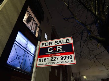 Stretford, İngiltere - 15 Kasım 2025: Manchester, İngiltere 'de bir tuğla bina üzerinde satılık tabelasıyla gece şehri sahnesi.
