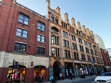 Manchester, İngiltere - 17 Kasım 2025: Süslü bir tarihi cephe, alışveriş mağazaları ve yayaların yer aldığı hareketli bir Manchester sokak sahnesi.