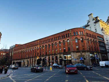 Manchester, İngiltere - 17 Kasım 2025: Temiz bir gökyüzü altında uzun kırmızı tuğlalı bina, trafik ve yayalarla dolu Manchester Portland caddesi.
