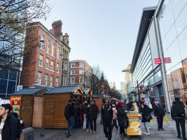 Manchester, İngiltere - 19 Kasım 2025: Manchester 'da ahşap tezgahlar, müşteriler ve yakınlarındaki çağdaş alışveriş merkezi ile hareketli pazar.