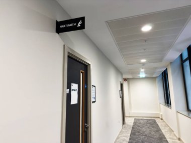 Manchester, İngiltere - 20 Kasım 2025: Kapısında siyah çoklu inanç işareti olan Manchester Üniversitesi koridoru, modern bir binada hafif ışıklandırma.