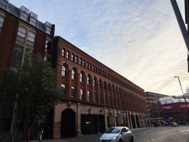 Manchester, İngiltere - 21 Kasım 2025: Bir dizi kemerli pencere ve tuğla cephe hattı alacakaranlıkta kalabalık bir Manchester caddesi.