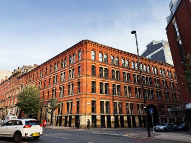 Manchester, İngiltere - 21 Kasım 2025: Manchester, İngiltere 'de tarihi kırmızı tuğla blok, Dickinson sokak sahnesini araçlar ve yayalarla dolduruyor.