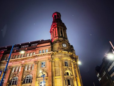 Manchester, İngiltere - 22 Kasım 2025: Karanlık gökyüzüne karşı aydınlatılmış bir saat kulesine sahip büyük Manchester binasının akşam manzarası.