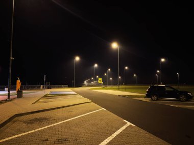 Polonya 'da sessiz bir gece sahnesi sokak lambaları, virajlı bir yol ve park halindeki bir SUV..