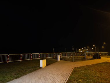 Polonya 'da gece sahnesi, metal bariyerler, sarı bir dolap ve kıvrımlı bir yürüyüş yolu boyunca parlayan sokak lambaları..