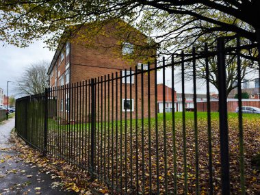 Brick apartment building with a tall iron fence and autumn leaves in Manchester.