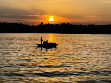 Gün batımında huzurlu bir nehrin üzerinde küçük bir teknede yaşayan insanların siluetleri..
