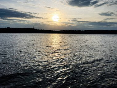 Sakin bir günbatımı, dalgalı sulara, siluetli kıyı şeridine altın yansıyor..