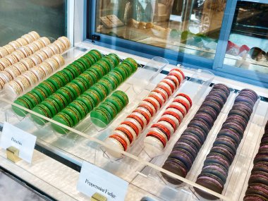Assorted pistachio green, peppermint fudge red white, and purple macarons arranged neatly in glass case.