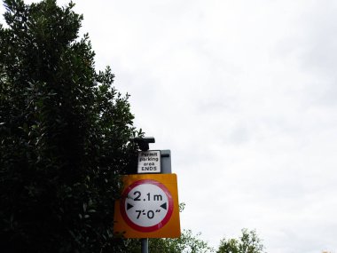 Yol kenarı tabelasında yükseklik sınırı ve park izninin Manchester caddesinde ağaçların yanında bittiği yazıyor..