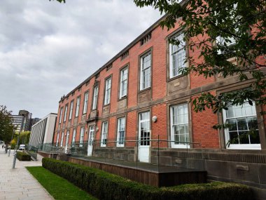 Camdan balkonu, ağaçları ve Manchester 'da modern şehir geçidi olan tuğladan bir kampüs binasının mimarisi.