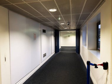 Beyaz duvarları, mavi halısı ve pencereleri olan bir Manchester ofis binasında parlak, boş bir koridor..