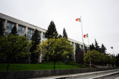 Chisinau, Moldova - 22 Kasım 2025: Chisinau Moldova 'daki hükümet binası, ağaçlar ve yeşil çimlerle çevrili uzun direkli bayraklar.