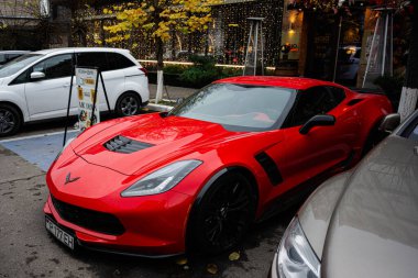 Chisinau, Moldova - 22 Kasım 2025: Parlak kırmızı bir Chevrolet Corvette coupe, Moldova 'nın Chisinau kentindeki işlek bir sokakta tatil dekorunun ortasında oturuyor