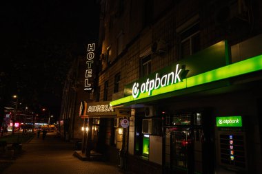 Chisinau, Moldova - 22 Kasım 2025: Chisinau Moldova 'da gece sahnesi neon otel tabelası, Adresa tabelası ve açık yeşil ot bankası vitrini.