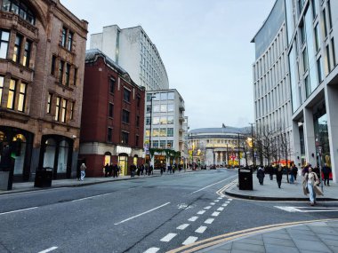 Manchester, İngiltere - 10 Aralık 2025: Tarihi tuğla binalar ve modern cam mağazaları karıştıran yayalar ve müşterilerle dolu Manchester Caddesi.
