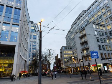 Manchester, İngiltere - 10 Aralık 2025: Çağdaş mimari, tramvay altyapısı, müşteriler ve akşam ışığı ile Manchester City Caddesi.