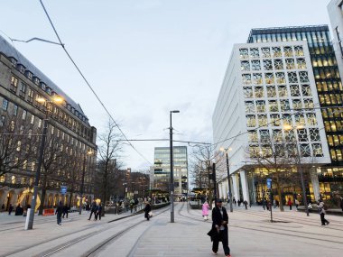 Manchester, İngiltere - 10 Aralık 2025: Çağdaş mimari, tramvay rayları ve yürüyen insanlarla dolu Manchester Plaza.