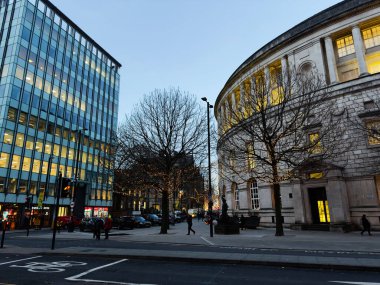 Manchester, İngiltere - 10 Aralık 2025: Manchester 'daki Alacakaranlık Şehir Peter Caddesi modern cam cephe, klasik mimari ve festival ışıklarını gösteriyor.