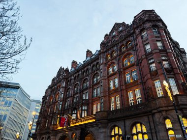 Manchester, İngiltere - 10 Aralık 2025: Parlak pencereler, bayraklar ve sıcak sokak ışıklandırması ile alacakaranlıkta Manchester binasını süsleyin.