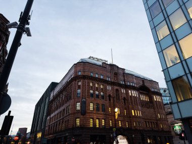 Manchester, İngiltere - 10 Aralık 2025: Manchester şehir merkezindeki tarihi kırmızı tuğlalı St Georges Binası modern cam cephe ve alacakaranlıkta aydınlanan sıcak pencereler.