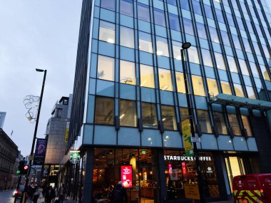 Manchester, İngiltere - 10 Aralık 2025: Manchester 'da modern cam bina zemin katında Starbucks ve dışarıda yayalar var.