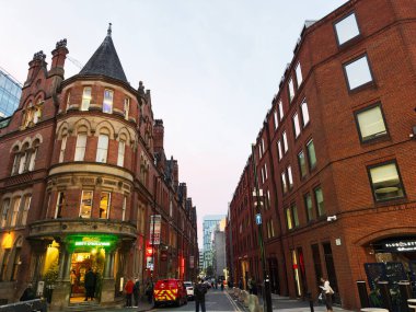 Manchester, İngiltere - 10 Aralık 2025: Canlı Manchester Lloyd sokak sahnesi alacakaranlıkta kırmızı tuğlalı mimari, dükkanlar ve yayalar.