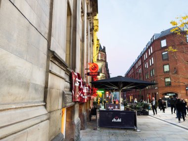 Manchester, İngiltere - 10 Aralık 2025: Manchester caddesindeki açık hava Tampopo kafe, neon ışıkları, şemsiyeler ve yayalar İngiltere 'de alacakaranlıkta.