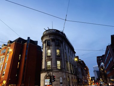 Manchester, İngiltere - 10 Aralık 2025: Manchester 'daki tarihi köşe binası, alacakaranlıkta John Dalton caddeleri ve ışıklarla kaplı tramvay hatları.