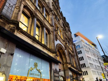Manchester, İngiltere - 10 Aralık 2025: Tarihi cephe, kafe ışıkları, Manchester, İngiltere 'deki kentsel cadde, sıcak parıltı ve mimari ayrıntı.