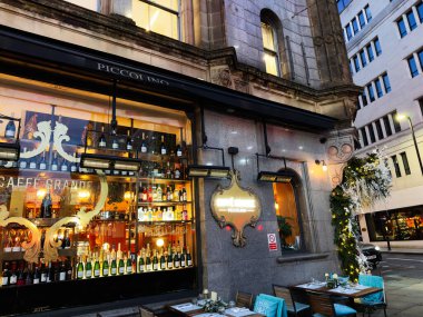 Manchester, İngiltere - 10 Aralık 2025: Manchester, İngiltere 'de bulunan Caffe Grande Piccolino cafe vitrininde şarap şişeleri, sıcak ışıklar ve şenlikli dekorasyon bulunmaktadır..