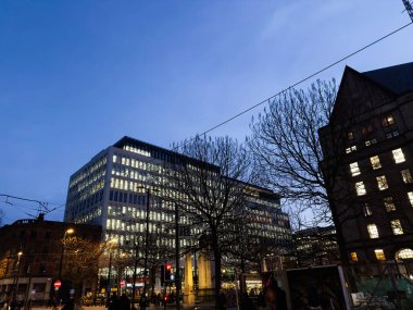 Manchester, İngiltere - 10 Aralık 2025: Modern cam ofis binası Manchester, İngiltere 'nin merkezinde canlı bir alacakaranlık sahnesini çerçeveler..